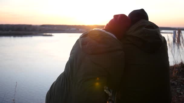 Dos personas están sentadas en la orilla del río, mirando y admirando la puesta de sol en el puente. cámara lenta, 1920x1080, full hd — Vídeos de Stock