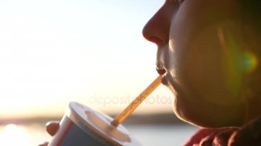 Şişman bir kız kemikleri ve lens etkisi ile gün batımında bir tüp ile soda içiyor. Slowmotion, Hd, 1920 x 1080