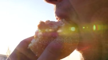Bir adam güneşin parlamasını ile büyük ve lezzetli hamburger yiyor yakın çekim. ağır çekim, 1920 x 1080, tam hd