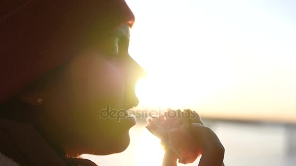 Una ragazza affamata mangia un delizioso hamburger succoso e non utile per strada nei raggi del tramonto con l'effetto di una lente. rallentatore, 1920x1080, hd completo — Video Stock