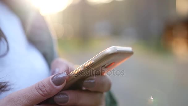 Девушка с телефоном в руках крупным планом на фоне заката, с размытием. slow motion, 1920x1080, полный привод — стоковое видео