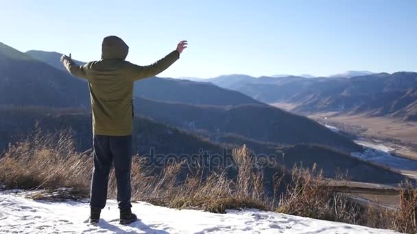 Молодий чоловік в куртці, стоячи на вершині гори, дивиться на відстань і відчуває свободу і радість від прекрасного пейзажу. повільний рух, 1920x1080, повний HD — стокове відео