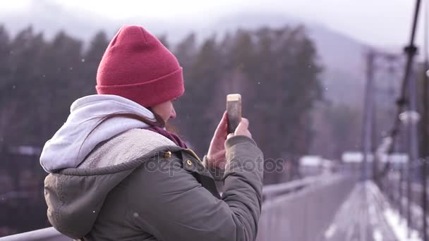 Ein Mädchen, das in einer Jacke auf einer Brücke steht, macht auf ihrem Handy ein Panorama der Landschaft. Zeitlupe, 1920x1080, full hd — Stockvideo