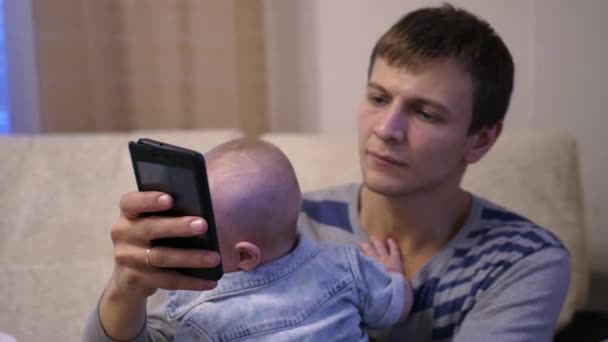 Il bambino è seduto con il padre tra le braccia, che tiene il telefono tra le mani, e quello che sta scrivendo su di esso. rallentatore, 1920x1080, hd completo — Video Stock