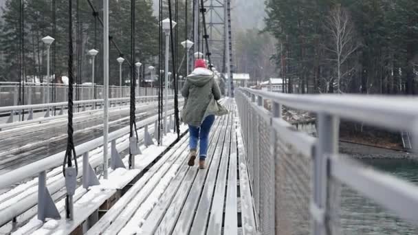 一个穿着夹克和帽子的女孩在冬天奔跑, 横跨横跨河的桥梁到公园。慢动作, 1920x1080, 全高清 — 图库视频影像