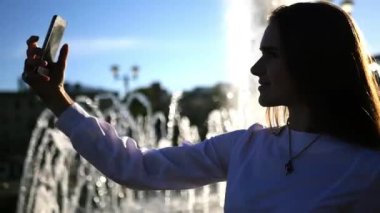 Uzun saç pozlar kamera, genç bir kızla bir lens etkisi ile şehrin çeşmenin fotoğrafını alır. HD, 1920 x 1080. ağır çekim.