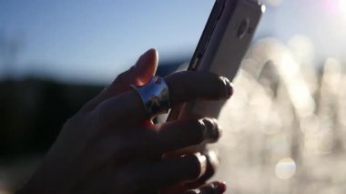 Kız, elinde telefon yakın çekim, arka plan ve güneş ışınlarının bir çeşme ile. HD, 1920 x 1080. ağır çekim.