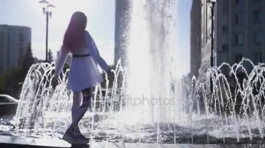 Güzel bir kız bir çeşme kenarında duruyor ve mutlu bir şekilde dönüyor. HD, 1920 x 1080. ağır çekim.