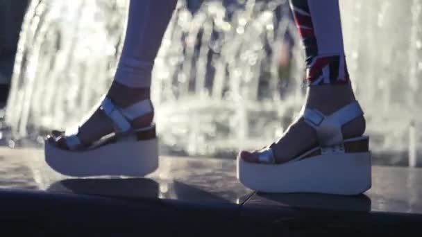 Beautiful legs in fashionable sandals on the edge of the fountain with glare and blurring of water. HD, 1920x1080. slow motion. — Stock Video