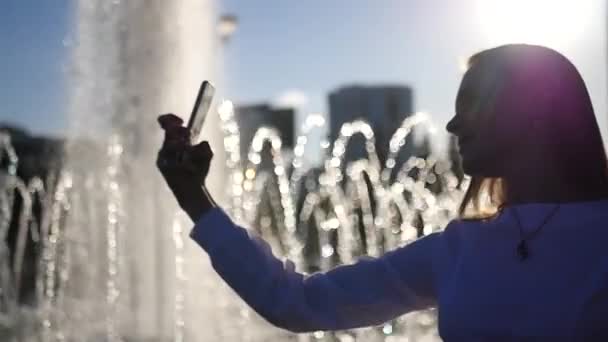 Chica joven con el pelo largo posando en la cámara, tomando una foto cerca de la fuente en la ciudad. HD, 1920x1080. cámara lenta . — Vídeo de stock