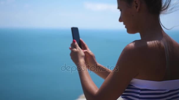 Красивая девушка с открытой спиной фотографирует синее море. HD, 1920x1080. замедленное движение . — стоковое видео