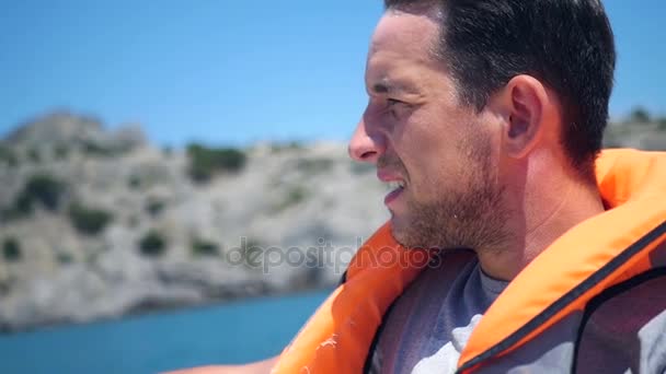 Een man in een zwemvest zeilen op een boot langs de kust. HD, 1920 x 1080. Slow motion. — Stockvideo