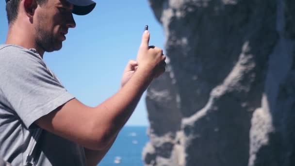 Un uomo simpatico scatta foto di rocce e onde nella macchina fotografica, mani nella vittoria gesto. HD, 1920x1080. rallentatore . — Video Stock