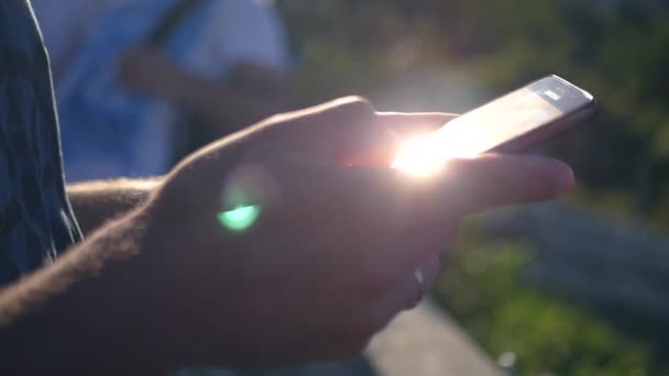 Une main d'homme avec un téléphone dans sa main, qui attrape les rayons du soleil et clignote dans l'appareil photo. HD, 1920 x 1080. au ralenti . — Video