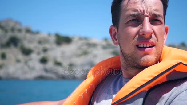 Un hombre en un chaleco en un barco entrecierra los ojos contra el sol brillante. HD, 1920x1080. cámara lenta . — Vídeo de stock