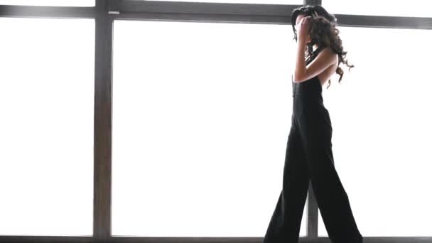 Cabelo castanho longo menina bonita na janela, photomodel vai caminha em vestido preto, branca bonita mulher caminha lentamente — Vídeo de Stock