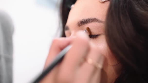 Макияж стилист делает Смоки глаза эффект для женщины на фотосессии, макияж для красивой кавказской модели, девушка приходит в салон красоты — стоковое видео