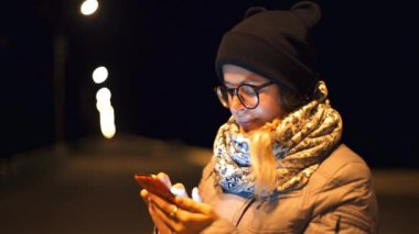 Kadın gülümsüyor telefonla gece saat açık havada onun smartphone, becerikli halklar hayat, kablosuz iletişim, duyguların iletileri okurken