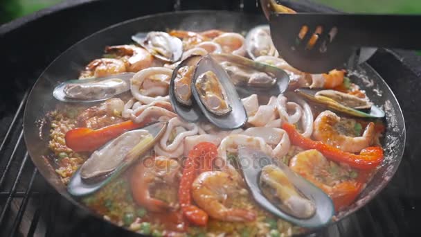 The cook makes paella on the open fire in the big hot pan, grill anf barbecue, spanish food, paella with seafood, food cooking outdoors — Stock Video