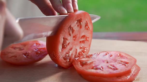 Кухар нарізає помідор гострим ножем на дерев'яній дошці на відкритому повітрі, роблячи овочевий салат, вегетаріанську страву, свіжі помідори з власного саду, готуючи на вулиці — стокове відео