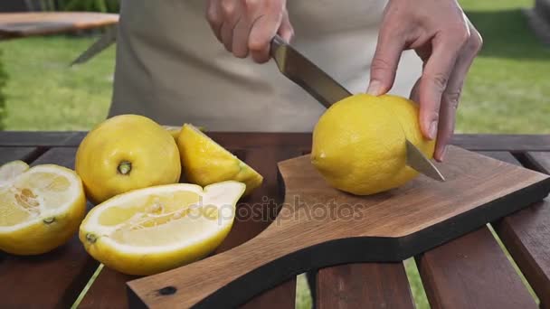 Повар разрезает лимон пополам на деревянной доске на открытом воздухе, делает фруктовый салат, посыпает лимонный сок, готовит на улице — стоковое видео