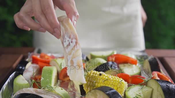 El cocinero hace ragú de verduras con trozos de bacalao de calabacín y berenjena con pimientos, comidas vegetarianas, cocinar verduras con pescado, cocina al aire libre — Vídeo de stock