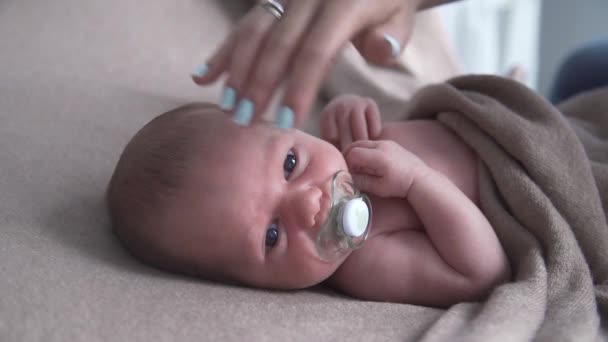 Bebê recém-nascido chupa chupeta em uma cama, mãe embala o bebê, a criança adormece — Vídeo de Stock