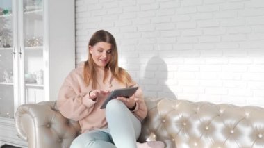 Genç kadın kanepede oturuyor ve tablet, online ödeme, online yardımcı, elektronik perifery kullanım kolaylığı internette sörf yapar, kız koltukta oturur ve ürünler online satın