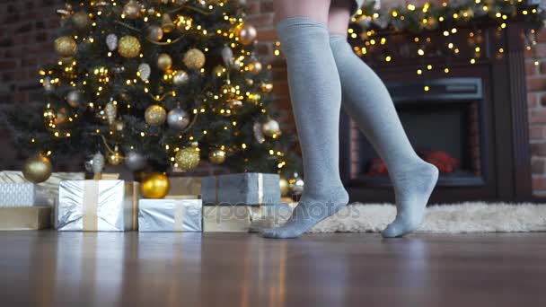 Ноги женщины в серых носках ходят возле рождественской елки и под ней подарки на Рождество, блестящая елка, гирлянды и балы, новогодние подарки, рождественские приготовления, канун Нового года — стоковое видео