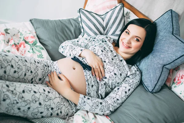 幸福美丽的孕妇在卧室里穿着睡衣的大肚皮, 未来的 parrents, 等待一个孩子, 母亲和照顾 — 图库照片