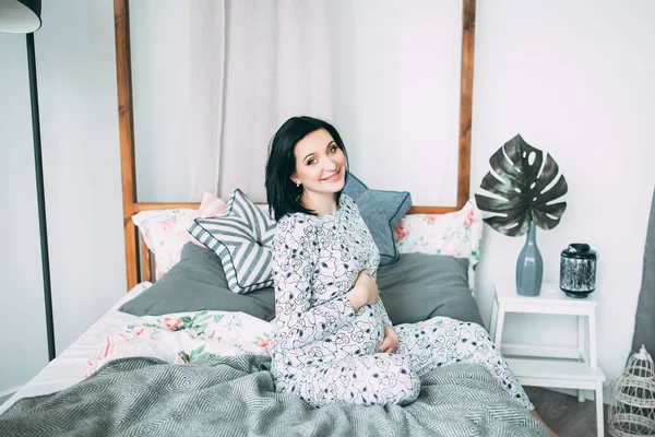 Happy beautiful pregnant caucasian woman with big belly in pajamas in the bedroom, future parrents, waiting for a child, motherhood and care — Stock Photo, Image