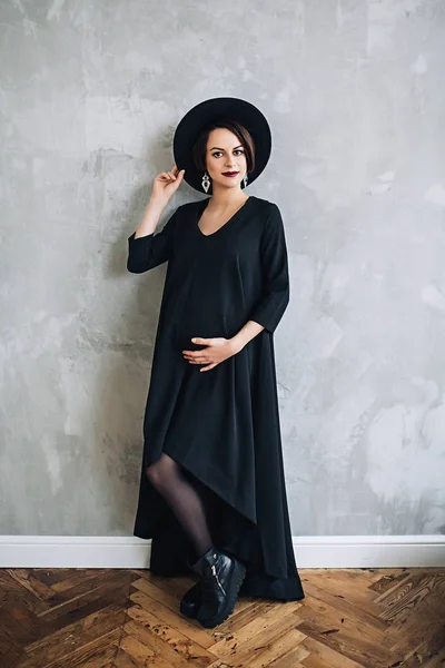 Mulher grávida branca com maquiagem em vestido preto e chapéu preto, retrato da futura mãe, gravidez feliz, retrato de moda, mulher de preto — Fotografia de Stock