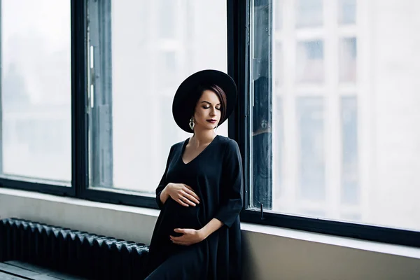 Femeie gravidă caucaziană cu machiaj în rochie neagră și pălărie neagră, portretul mamei viitoare, sarcină fericită, portret de modă, femeie în negru — Fotografie, imagine de stoc