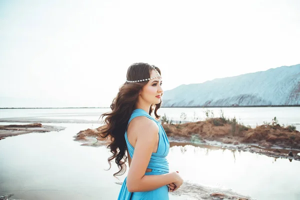Portrait of the attractive caucasian woman with long dark hair, pretty girl in the blue dress and with diadem in the hair against the beautiful background of the landscape, woman near the lake and