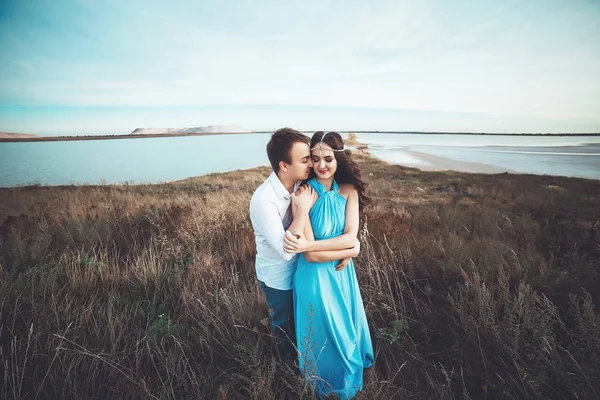 Young couple in love is resting together near the lake and mountains, beautiful caucasian woman and man fell in love, tenderness and hugs, straight couple against the beautiful background of the