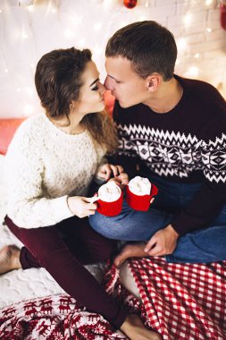 Kazak giymiş çift öpüşme ve sarılma mutlu Noel ağacının yanında rahat bir atmosfer ve aşk, ev ve aile, beyaz çift, evli insanlar