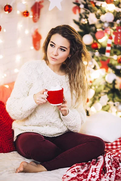 Kadın sıcak çikolata ile Noel ağacı yakınındaki oturur kazak, atmosferde tatil ve çelenk güzel kadın, güzel beyaz kadın