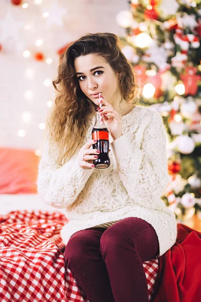 Femeia stă lângă pomul de Crăciun cu unt de băutură cola, femeie frumoasă în pulover, atmosferă de vacanță și ghirlande, femeie albă frumoasă — Fotografie, imagine de stoc