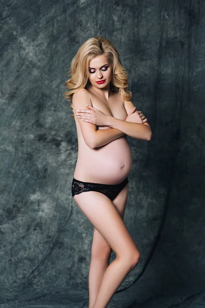 Frumoasa femeie atractivă este gravidă, gravidă femeie albă cu păr lung blond creț în lenjerie intimă neagră, frumusețea femeii însărcinate, portret sexy — Fotografie, imagine de stoc