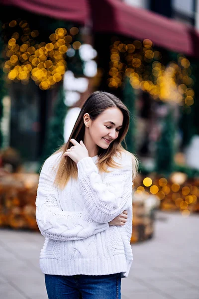 Happy white girl with long dark hair in sweater, garlands in bokeh, holiday cozy atmosphere, smiling woman with bengal lights, outdoors portrait — Stock Photo, Image