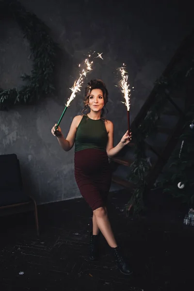 Caucasian pregnant woman with make up and curly hair holds sparkling fireworks, portrait of future mother, happy pregnancy, fashion portrait, stylish pregnancy