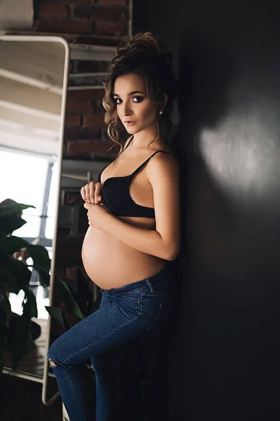 Gelukkig mooie zwangere Kaukasische vrouw met grote buik in zwarte ondergoed zit op het bed in de slaapkamer, toekomstige parrents, wachten op een kind, moederschap en zorg — Stockfoto