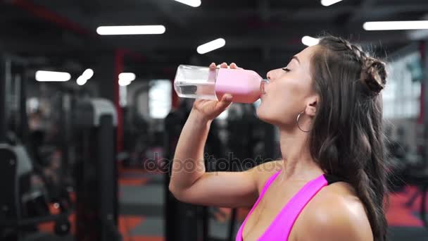 美丽迷人的女人喝水从瓶子在健身房后辛勤工作的模拟器, 妇女休息后锻炼, 运动和锻炼, 健身房在体育俱乐部 — 图库视频影像