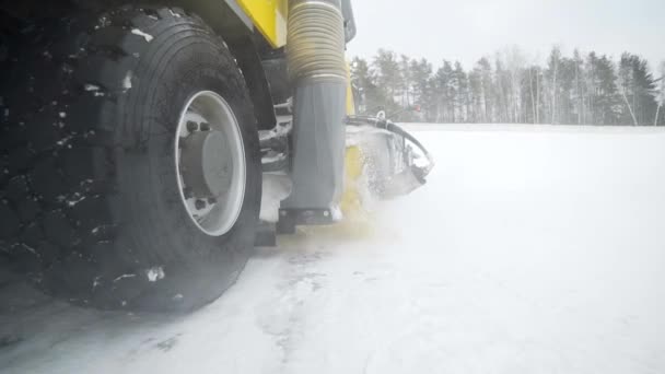 Камера слідує за важкою колісною технікою, яка виводить сніг з дороги з великим масивним обертовим пензлем у сніжну погоду, спеціальним обладнанням для прибирання доріг, прибирання снігу та льоду, спеціалізується — стокове відео