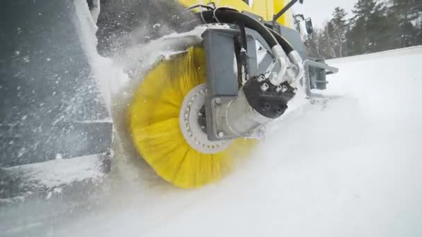 El cepillo amarillo de la nieve y el camión de eliminación de hielo está girando y eliminando la nieve de la carretera, la maquinaria de cosecha con ruedas elimina la nieve de la carretera con un gran cepillo giratorio masivo en el clima nevado — Vídeo de stock