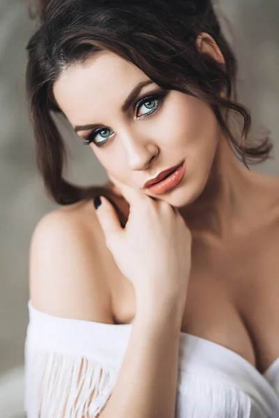 Porträtt av vackra attraktiva sexig kvinna i vitt med mörkt hår, blå ögon och sensuella röda läppar står i vit klänning med djup urringning öppna brest Stockbild