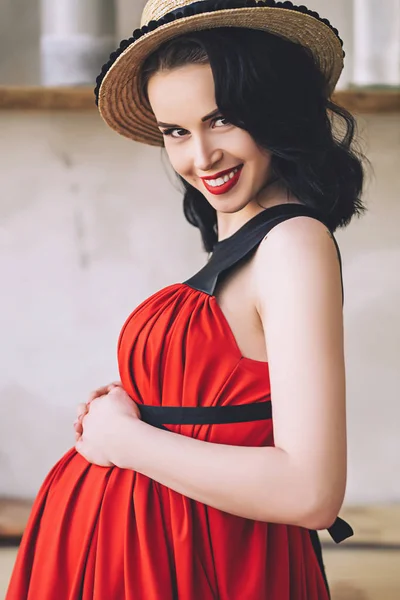 Portret de modă de femeie gravidă atractivă elegantă în sarafan roșu lung și pălărie de paie, fotografia femeii însărcinate fericite și frumoase, devenind papagali, haine elegante pentru sarcină, viitoarea mamă — Fotografie, imagine de stoc
