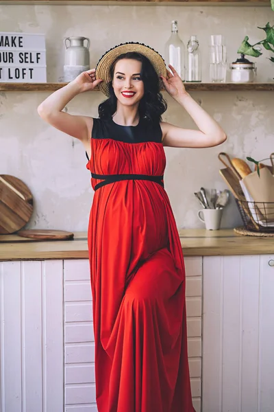 Retrato de moda de senhora grávida elegante atraente em sarafan vermelho longo e chapéu de palha, foto da mulher grávida feliz e bonita, tornando-se pais, roupas elegantes para a gravidez, futura mãe Imagens De Bancos De Imagens