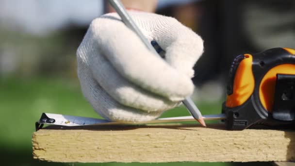 Primo piano dell'uomo in guanti da lavoro che misura il blocco di legno dalla roulette e lo segna a matita prima di fare il taglio, roba di legno fatta a mano, fabbricazione di prodotti in legno all'aperto, cose fai da te a casa — Video Stock