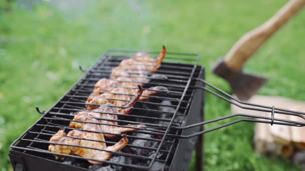 Primo piano delle ali di pollo arrosto fumante caldo sul calore del barbecue, barbecue nel cortile nella verde giornata estiva, cucinare all'aperto sul fuoco aperto — Video Stock